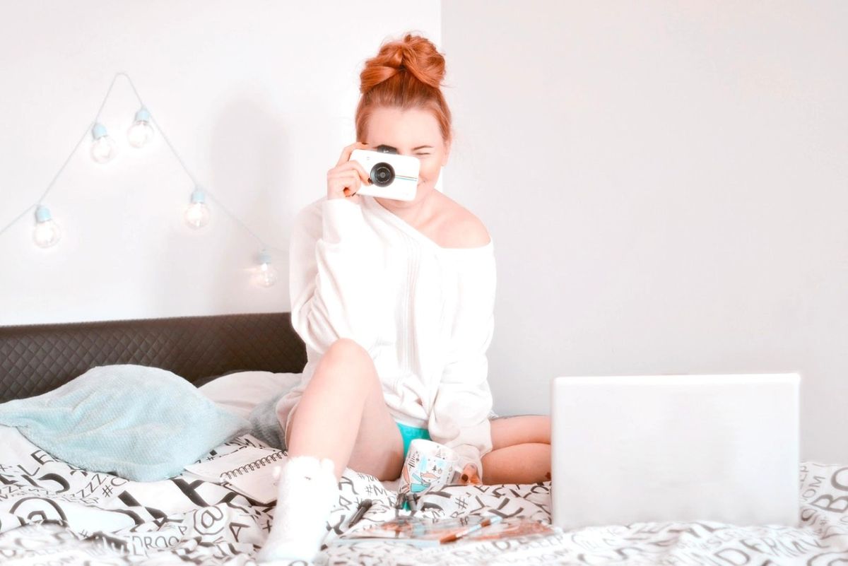 Frau sitzt mit Laptop und Kaffetasse im Bett und fotografiert