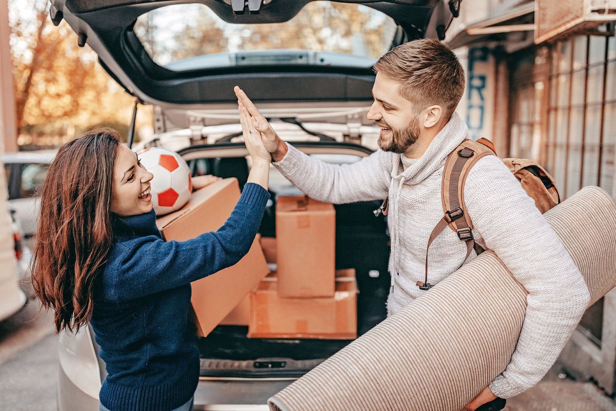 Junges Paar klatscht sich ab vor dem Auto mit Kisten