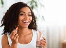 Junge farbige Frau mit einem Glas Wasser und Interdentalbürste