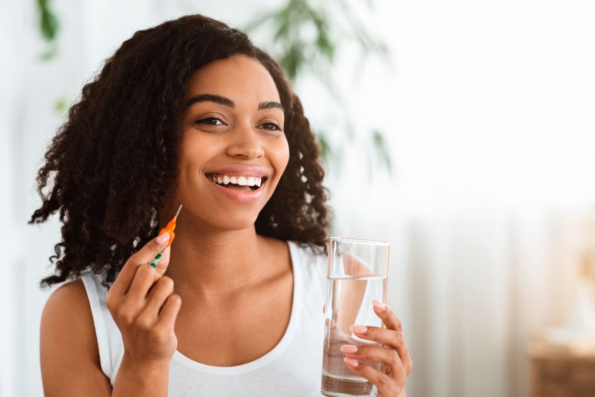 Junge farbige Frau mit einem Glas Wasser und Interdentalb&uuml;rste