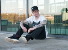 Mann mit Skateroutfit sitzt vor Glasfenster