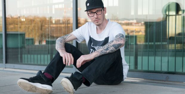 Mann mit Skateroutfit sitzt vor Glasfenster