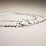 Close-up of a silver chain bracelet with a heart-shaped clasp stamped 925 on a pale beige surface.