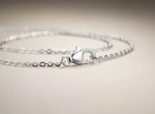 Close-up of a silver chain bracelet with a heart-shaped clasp stamped 925 on a pale beige surface.