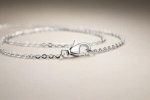Close-up of a silver chain bracelet with a heart-shaped clasp stamped 925 on a pale beige surface.