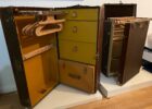 Open vintage Louis Vuitton suitcases with yellow interiors, showing wooden clothes hangers inside on a white shelf