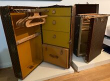 Open vintage Louis Vuitton suitcases with yellow interiors, showing wooden clothes hangers inside on a white shelf