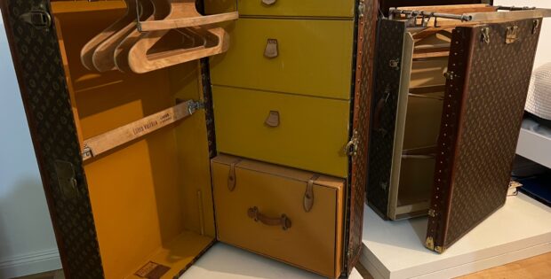 Open vintage Louis Vuitton suitcases with yellow interiors, showing wooden clothes hangers inside on a white shelf